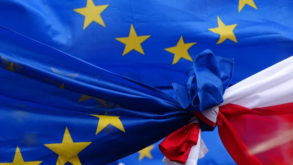 EU-Flagge und Polen-Flagge verknoten sich in der Mitte des Bildes